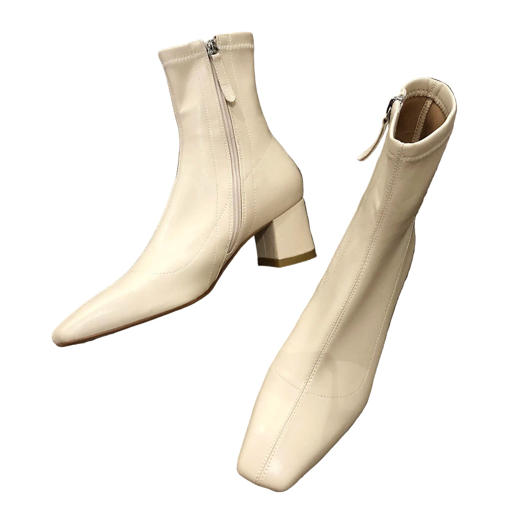 Pair of white ankle boots with a block heel on a gray surface