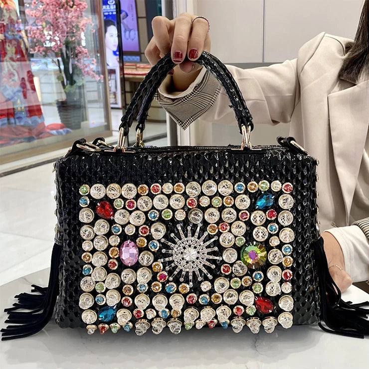 Black handbag with colorful gemstones held by a person indoors.